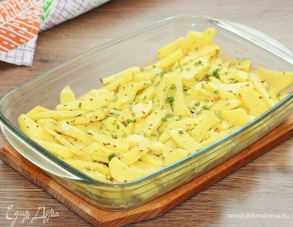 Очищенный и нарезанный брусочками картофель выкладываем в форму для запекания. Добавляем нарезанный полукольцами лук (0,5 шт.), порубленный укроп (0,5 пуч.) и чеснок (1 зуб.), 3 ст. л. подсолнечного масла и приправу для картофеля (1 ч. л.), солим и перчим. Перемешиваем картофель так, чтобы он был покрыт маслом.