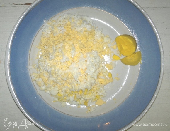 Яйца сварить вкрутую, остудить в холодной воде. Вареные яйца почистить. Немного желтка отложить для украшения. Яйца натереть на мелкой терке.