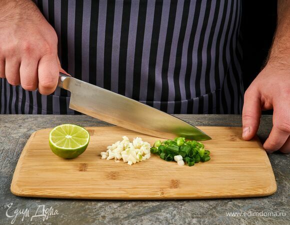 Займитесь приготовлением соуса. Измельчите зеленый лук и чеснок. Переложите в ступку.