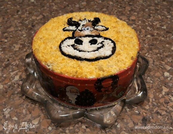 Достаем салат из холода, движением вверх снимаем кольцо. Украшаем салат символом года. Контур бычка — маслины, тонко нарезанные на полоски. Чтобы бычок был белым, натрем немного яичного белка. Пятна на морде — молотый грецкий орех. Для яркости картинки на фоне выложен тертый яичный желток.