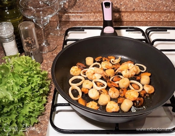 Морепродукты откинуть на сито. Зубчик чеснока очистить, нарезать на пластины. Нагреть сковороду, влить оливковое масло и обжарить чеснок. Когда чеснок станет черным, выбросить его, а в чесночное масло положить морепродукты и обжарить их одну минуту.