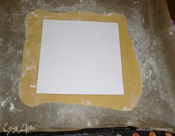 Медовую лепешку выкладываем на коврик для выпечки. Используя бумажный шаблон, обрезаем края.
