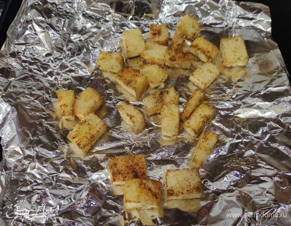 Готовим сухарики: хлеб разрезаем на кусочки, сбрызгиваем оливковым маслом, посыпаем солью, перцем, паприкой и по желанию сушеным чесноком. Отправляем в духовку на 5–7 минут при 180°C.