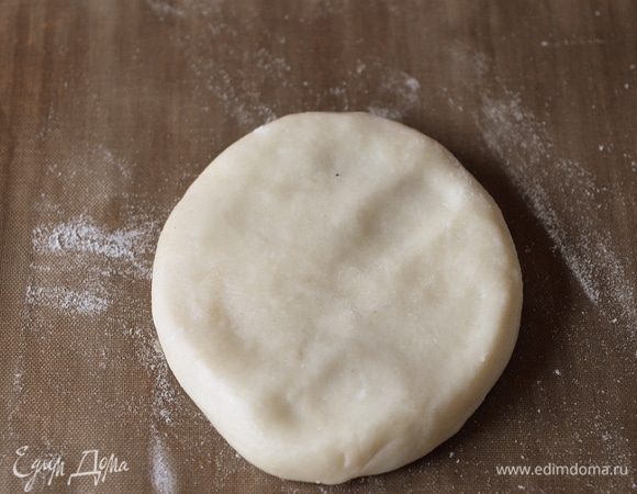 Формирование рулетов. Каждый раз тестовые заготовки выкладываем в холодильник во временном порядке. Все заготовки накрывать пищевой пленкой! Кладем колобок в холодильник на место взятого белого или цветного шарика (как удобнее) швом вниз. Проделываем эти же манипуляции с оставшимися шариками. В холодильнике по итогу будут лежать 11 белых шариков из теста. Скалку посыпать мукой. Берем шарик, который мы положили в холодильник первым. Другие пока за это время успеют отлежаться. Расплющиваем его ладонью.