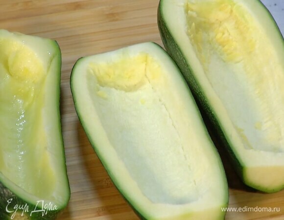 Цукини разрезать вдоль пополам и ложкой вынуть сердцевину с семенами, чтобы получились лодочки.