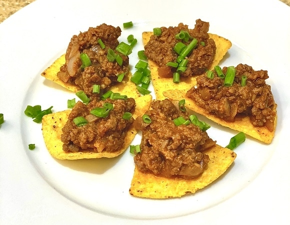 Выкладываем кукурузные чипсы на тарелку, сверху — фарш. Посыпаем зеленым луком.