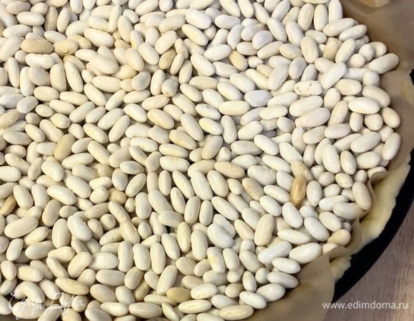 Достаньте тесто из холодильника, равномерно распределите по форме. Сверху положите лист пергамента, а на него груз (фасоль, горох). Выпекайте основу в разогретой духовке при 180°C 20 минут. Затем уберите груз и выпекайте еще 15 минут, до золотистости.