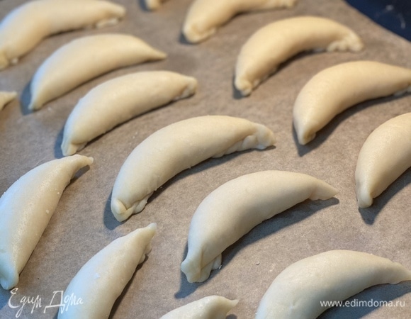 Духовку разогреть до 170°C. Каждый шарик раскатать в овал, положить 1,5 ч. л. начинки и защипнуть края, как на вареники. Подогнуть края вниз и придать изделиям форму полумесяца. Выложить на застеленный пергаментом противень.