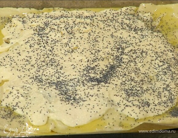 Один пласт теста выложить на выстеленный бумагой для выпечки противень, сверху, немного отступая от краев, разложить обжаренные яблоки, затем накрыть вторым пластом теста, смазать его растопленным сливочным маслом, сверху, так же слегка отступая от краев, равномерно распределить творожную начинку и посыпать 1 ч. ложкой мака.