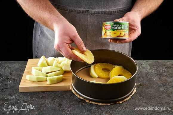 С колец ананаса в соке Del Monte слейте жидкость. Застелите форму пергаментом. Выложите дольки яблок и кольца ананасов.