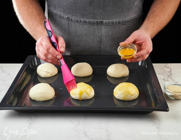 Из поднявшегося теста сформируйте шесть булочек. Выложите заготовки на противень, смажьте каждую яичным желтком и посыпьте кунжутом. Запекайте в духовке, разогретой до 190°C, около 18 минут.