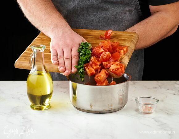 Приготовьте красный соус. Помидоры нарежьте средним кубиком, чеснок и базилик мелко порубите. Переложите в сотейник, влейте оливковое масло. Поставьте на огонь, посолите. Тушите, постоянно помешивая, до состояния соуса.