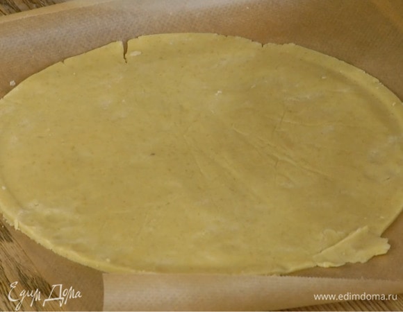 На присыпанной оставшейся мукой рабочей поверхности сделать из теста шар, поместить его между двумя листами бумаги для выпечки и раскатать в тонкий пласт, затем сформировать из него круг.