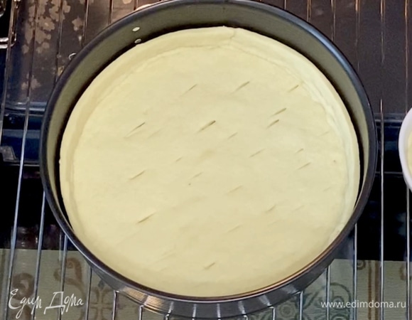 Достать тесто из холодильника, вырезать по форме дно и края высотой 3 см. Сначала уложите дно в форму, а затем — края, соедините по нижним бортам. Сделайте несколько проколов вилкой или ножом. Отправьте в духовку на 15 минут при 180°C