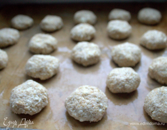 Смочить руки водой. Скатать из теста шарики и слегка приплюснуть их сверху на смазанной бумаге для выпечки.