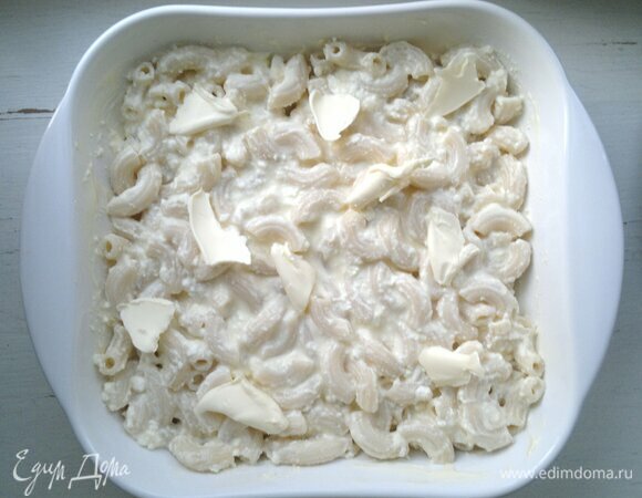 В форму выложить макароны с творожной массой, ложкой слегка уплотнить. Оставшееся сливочное масло нарезать мелкими кусочками и выложить сверху.