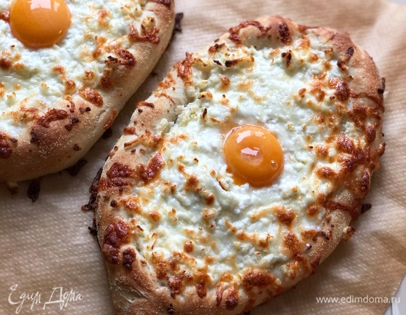 Выпекать хачапури удобнее по 2 шт., в процессе выпекания они сильно увеличиваются в размере и как бы набухают. Когда хачапури уже готовы (они очень хорошо подрумянились, сыр расплавился, а на тесте стали появляться небольшие подпалины), примерно через 10–15 минут, сделать вилкой небольшое углубление в сыре и аккуратно положить туда целый желток. Снова убрать в духовку на 30–60 секунд. Желток должен остаться абсолютно жидким. Готово!<br />
Достать хачапури из духовки и подавать горячими немедленно, отламывая от бортиков тесто, макая в желток и расплавленный сыр. Приготовить таким же образом оставшиеся хачапури.