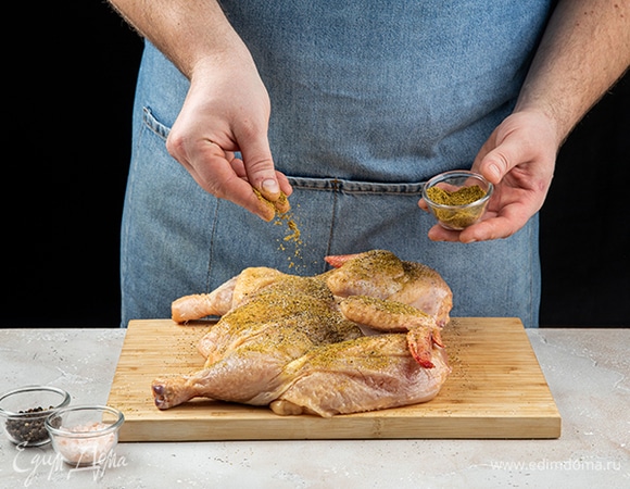 Цыпленка разрежьте по линии грудки. Смешайте хмели-сунели, соль и перец. Натрите этой смесью цыпленка со всех сторон.