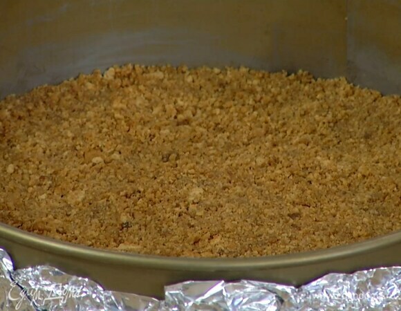 Дно и бока разъемной формы плотно обернуть фольгой, выложить печенье и плотно утрамбовать в корж, затем отправить в холодильник.