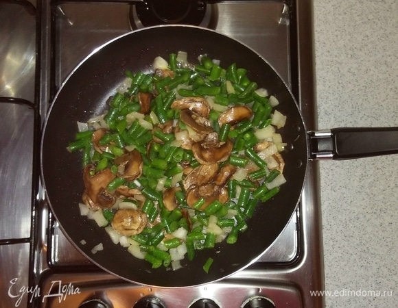Затем добавляем к луку и шампиньонам стручковую фасоль. Перемешиваем и обжариваем все вместе еще 10 минут. Затем снимаем с огня.