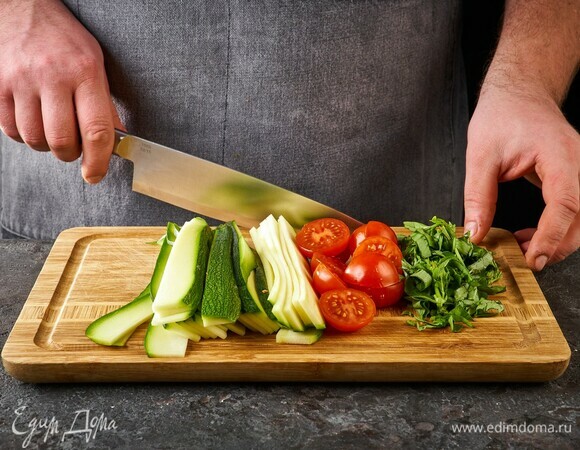 Теркой для корейской моркови или ножом для чистки овощей нарежьте цукини на тонкие длинные полоски. Черри разрежьте пополам, нарежьте крупно базилик.