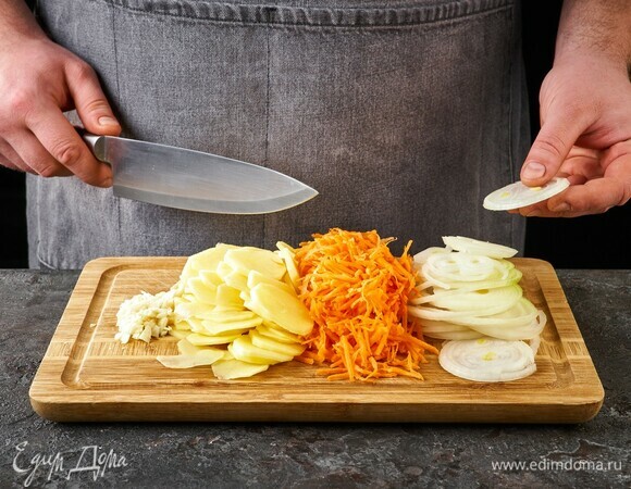 Картофель нарежьте тонкими кружочками. Морковь натрите на крупной терке, лук нарежьте тонкими кольцами, чеснок мелко порубите.