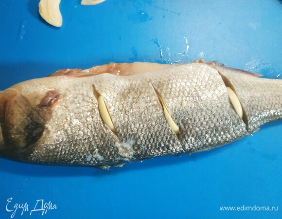 Рыбу промыть, очистить от чешуи и внутренностей. Обрезать плавники. Сделать надрезы с обеих боков. Хорошенько натереть смесью соли и перца. В разрезы вставить нарезанный пластинами чеснок.