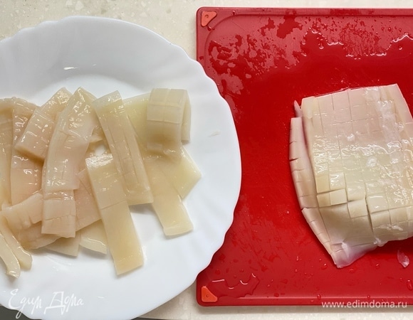 Кальмары — пополам, чтобы получились квадратные кусочки. Перевернуть и с внутренней стороны сделать аккуратные надрезы сеточкой. Главное, чтобы кусочки остались целыми. Затем нарезать на кусочки размером 3x6 см. Вместо кальмаров можно использовать креветки.