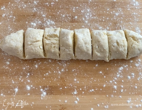 Рабочую поверхность посыпаю мукой и выкладываю на нее тесто. Затем раскатываю тесто в колбаску и делю ее на 8 равных частей. Также можно разделить тесто на 12 частей.