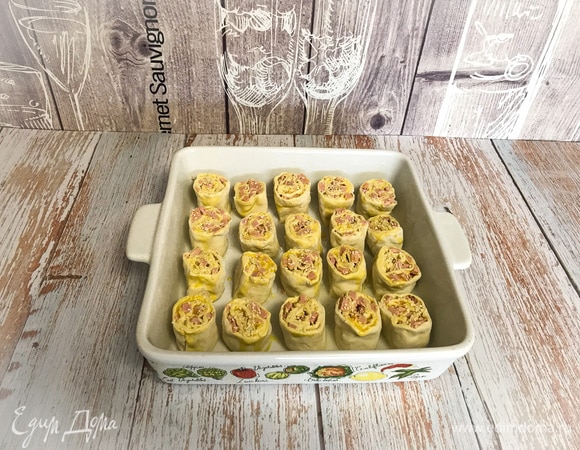 Сворачиваем тесто с начинкой в рулет, нарезаем небольшими кусочками, выкладываем в форму для выпечки. Сверху смажьте яйцом. Выпекать 25 минут в разогретой до 180°C духовке. Готовые булочки можно посыпать кунжутом!