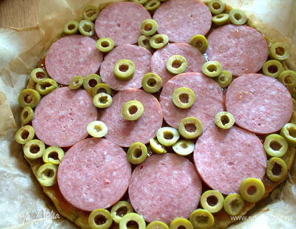 Основу смазать кетчупом или соусом «Сладкий чили», сверху выложить сервелат и оливки.