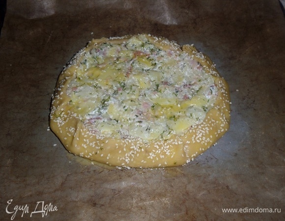 Края лепешки приподнимаем вверх и укладываем на начинку, делая небольшие защипы. Смазываем пирог яичным желтком и посыпаем кунжутом. Отправляем в разогретую духовку.