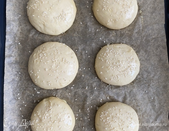 Ставим опару: соединить дрожжи, теплое молоко, воду и сахар. Все перемешать и оставить в тепле на 20 минут, до образования пенистой шапочки. Сливочное масло растопить, остудить до комнатной температуры. Взболтать вилкой яйцо. Соединить опару, яйцо, масло. Добавить муку и замесить однородное тесто. Готовое тесто мягкое, эластичное, не липнет к рукам. Муки больше, чем указано в рецепте, не добавляем. Миску смазать растительным маслом, положить в нее тесто, затянуть пищевой пленкой и убрать в тепло на 1,5 часа. Спустя время тесто обмять, разделить на шесть равных частей. Разложить на противень, застеленный пергаментом, накрыть пленкой и убрать еще на 30 мин. Духовку разогреть до 180°C. Смазать булочки смесью желтка и 1 ч. л. молока, посыпать кунжутом.