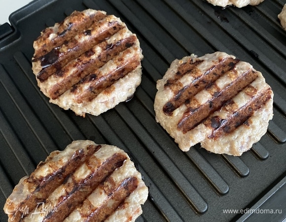 Пока пекутся булочки, готовим котлеты. Мясо перекрутить в фарш вместе с луком, чесноком, добавить специи по вкусу и хорошо вымешать. Разделить на шесть частей, сформировать плоские котлеты, обжарить на сильном огне по 4–5 минут с каждой стороны (можно использовать гриль или сковороду). Отложить в теплое место до момента сборки.