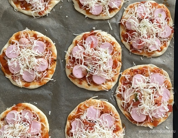 Смазать основу соусом, посыпать тертым сыром, разложить сосиски, тонко нарезанные помидоры, сверху еще немного посыпать сыром.