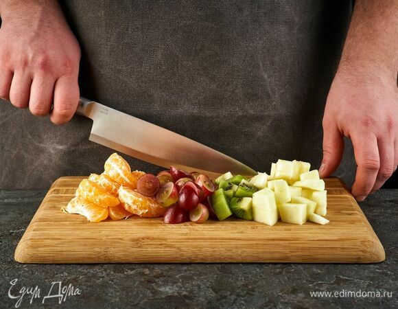 Яблоко и киви нарежьте кубиками. Ягоды винограда разрежьте на половинки, очистите от косточек. Мандарины почистите и разделите на дольки.