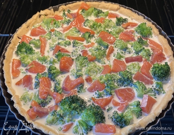 Достать песочную основу из духовки, посыпать тертым сыром, сверху выложить начинку и залить все сливочной заливкой.