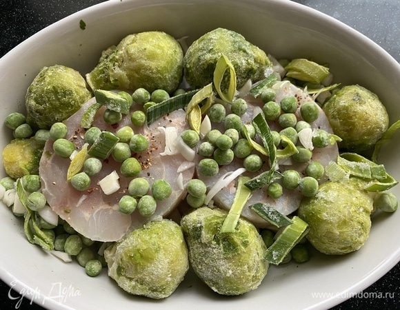 Сверху рыбы выкладываем замороженные брюссельскую капусту и зеленый горошек. Затем — мелко нашинкованный чеснок и лук-порей, нарезанный колечками. Перчим.