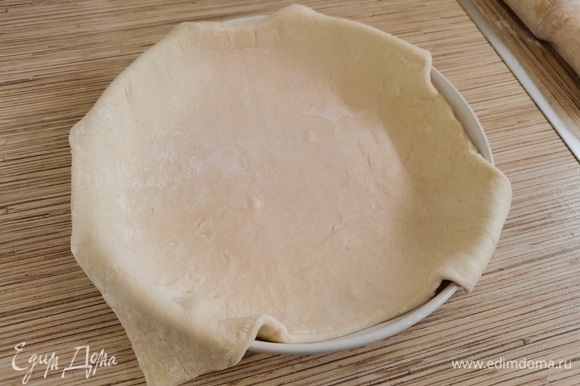 Тесто разморозить, раскатать и выложить в форму, чтобы края свисали. Дно застелить пекарской бумагой или смазать растительным маслом. Размер моей формы — 21 см.