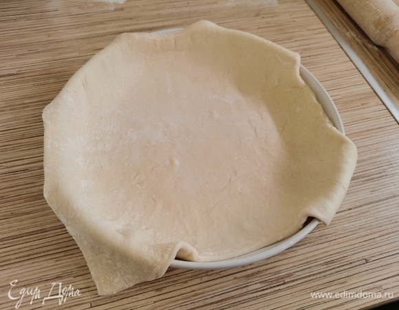 Тесто разморозить, раскатать и выложить в форму, чтобы края свисали. Дно застелить пекарской бумагой или смазать растительным маслом. Размер моей формы — 21 см.