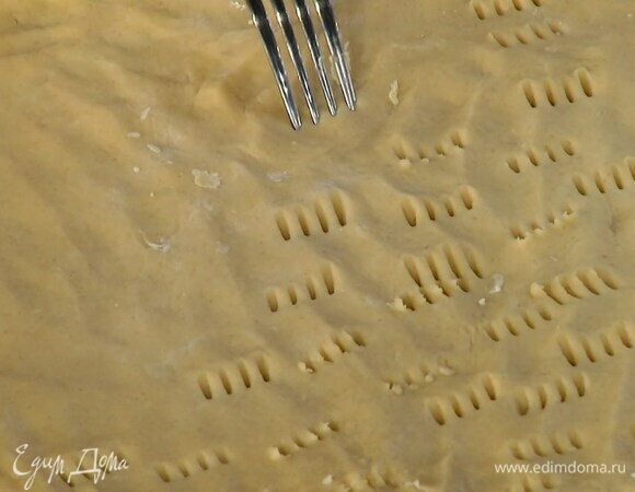 Выложить тесто на выстеленный бумагой для выпечки противень, равномерно распределить руками в тонкий пласт и часто наколоть вилкой.