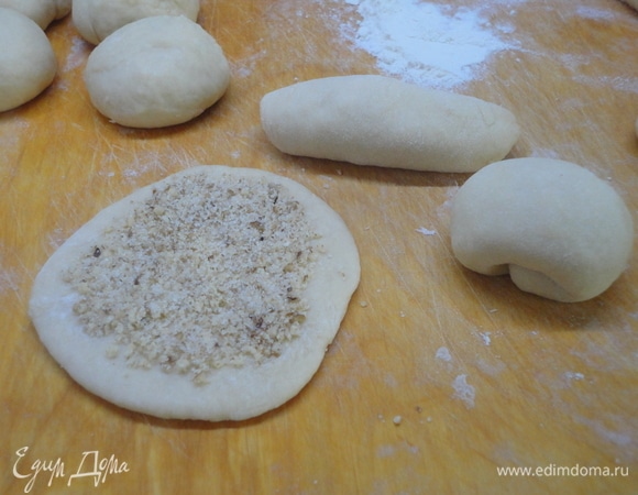 Тесто выложите на стол, подпыленный мукой, и разделите на небольшие кусочки по 60 г. Каждый раскатайте и выложите на лепешечку по 1 ч. л. смеси орехов с сахаром. Сверните рулетиком и затем подверните края, формируя булочку. Выложите в форму, смазанную сливочным маслом, и оставьте на расстойку. Разогрейте духовку до 180°C.