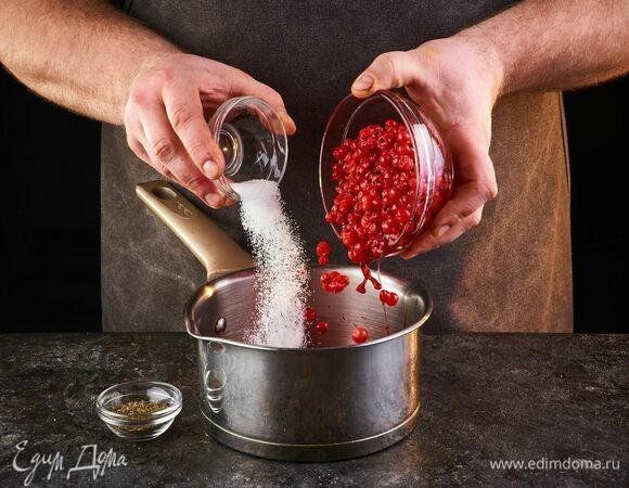 Приготовьте соус. Ягоды красной смородины промойте и снимите с веточек. Выложите в сотейник, всыпьте сахарный песок. 