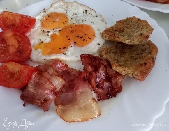 Одна порция завтрака с яичницей, беконом и томатами.