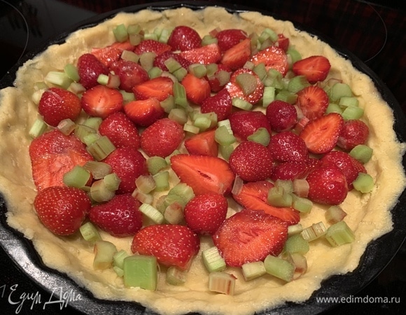 В форму с тестом выложите ягоды клубники и нарезанный кусочками ревень.