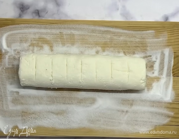 Доску посыпаем мукой и выкладываем творожную массу. Формируем колбаску и разрезаем на равные части.