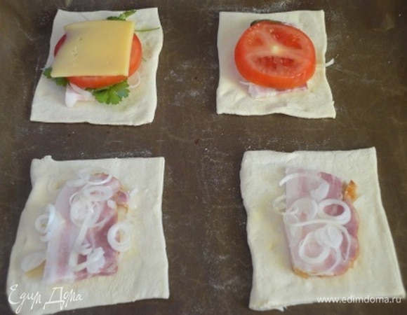 Каждый пласт размороженного слоеного теста раскатать и разделить на 6 прямоугольников. На 6 кусочков теста выложить по кусочку бекона, сверху — кружочки лука, затем — листики любимой зелени, кружочек помидора и сверху сыр. Края теста смазать белком.