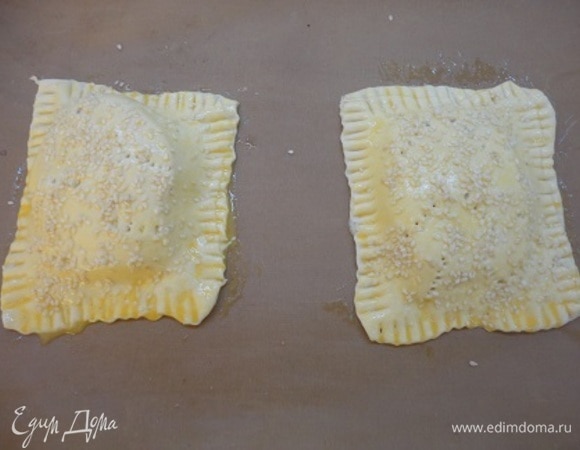 Наколоть вилкой. Скрепить верхние и нижние кусочки теста с помощью вилки и смазать желтком. Посыпать кунжутом.