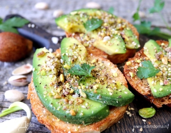 Ломтик батона натереть чесноком. Сверху положить ломтики авокадо. Щедро посыпать ароматной фисташковой крошкой. Полить оливковым маслом, добавить несколько кристаллов крупной соли, посыпать свежемолотым перцем. Украсить листиками петрушки, кинзы или руколы.