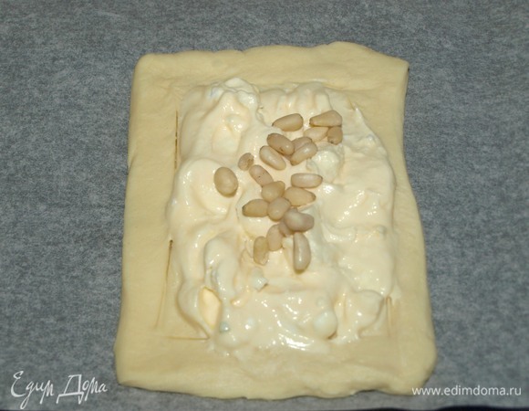 Мягкий соленый сыр смешать с яичным желтком. Если сыр не соленый, то добавьте соль по вкусу. Выкладываем сыр на тесто в обозначенных границах, сверху посыпаем кедровыми орехами.